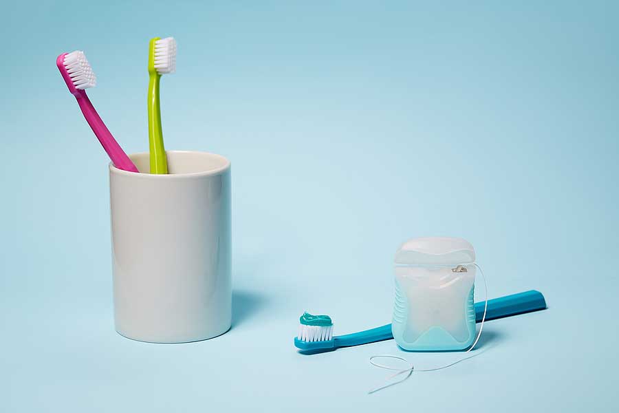Two toothbrushes in a cup with a case of floss and another toothbrush next to the cup.